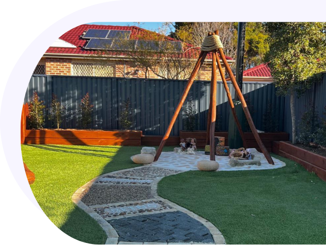 A modern childcare center outdoor play area featuring a large wooden teepee frame, a curved stone sensory pathway, artificial green grass lawns, and a raised wooden garden bed.